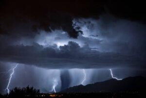 %Imagetitle% | Bumble Breeze Plumbing, Heating &Amp; Air Lightning streaks across a dark night sky beneath thick storm clouds, illuminating rain falling over distant mountains and a barely visible landscape below.