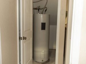 %Focuskw% | Bumble Breeze Plumbing, Heating &Amp; Air A water heater is installed in a small utility closet with white walls and a partially open door. Pipes are connected at the top of the unit.