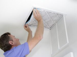 %Focuskw% | Bumble Breeze Plumbing, Heating &Amp; Air A man in a blue shirt replaces an air filter in a ceiling vent, with the vent cover open and his hands holding the filter in place.