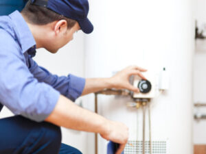 %Imagetitle% | Bumble Breeze Plumbing, Heating &Amp; Air A person wearing a blue uniform and cap adjusts the settings on a water heater, focusing on the control panel.