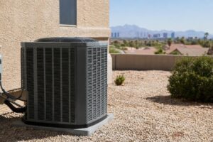 An outdoor air conditioning unit sits on gravel beside a building, with desert plants and a city skyline visible in the background.